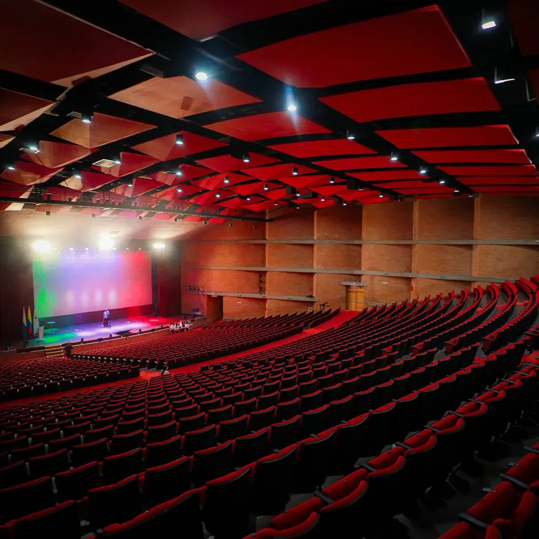 Sala del Teatro Universidad de Medellín, con sillas rojas en gradería frente al escenario.